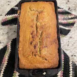 A warm loaf of banana bread rests in a cast iron pan.