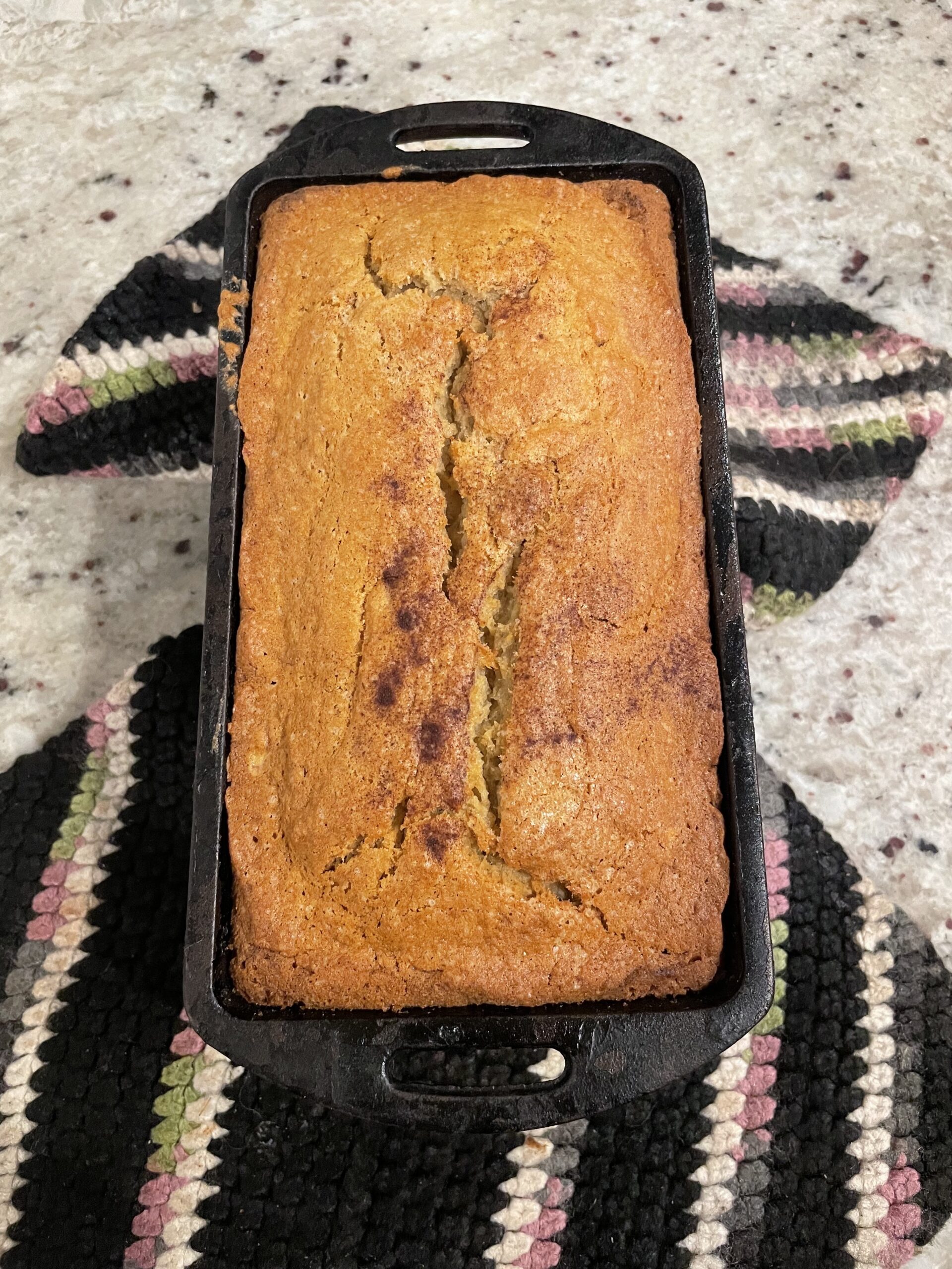 A warm loaf of banana bread rests in a cast iron pan.